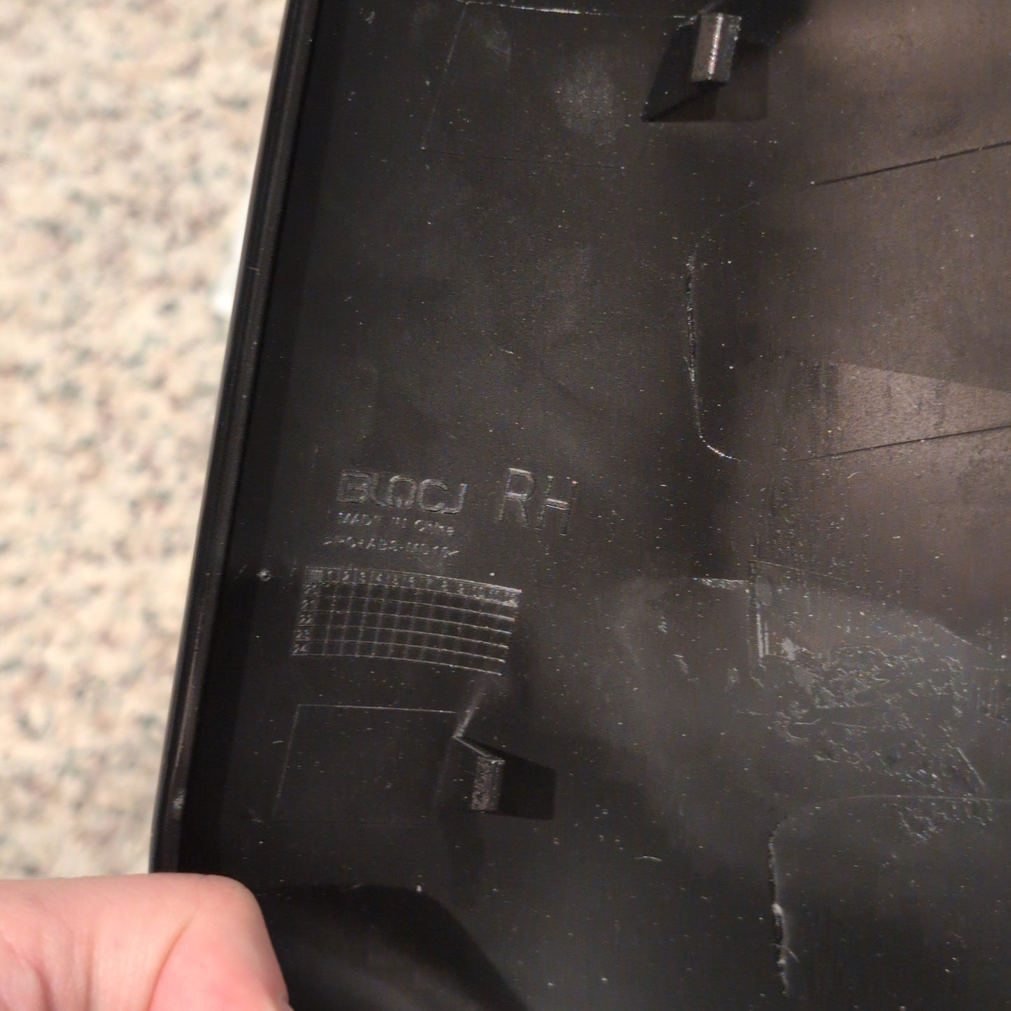 Close-up of a black electronic device with a hand holding a tool on a textured surface.